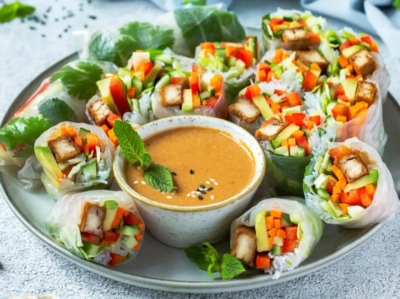 Frische Sommerrollen gefüllt mit Gemüse und Tofu, serviert mit cremiger Erdnusssauce. Ein leichter Genuss für warme Tage.