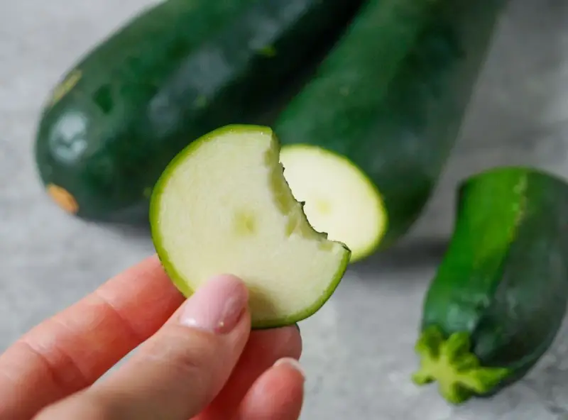 Frische Zucchini roh essen ist gesund und lecker. Eine Hand hält ein Stück, das angeknabbert ist.